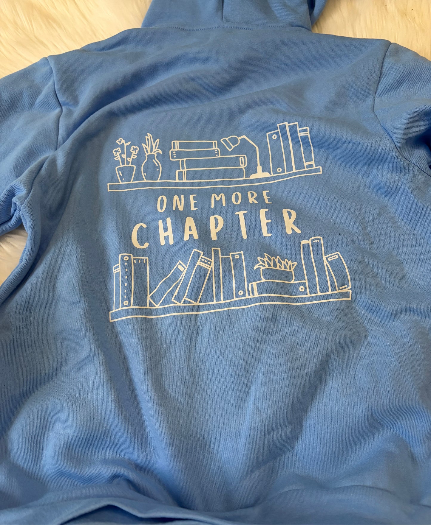 Blue hoodie with 'One More Chapter' design on a white surface